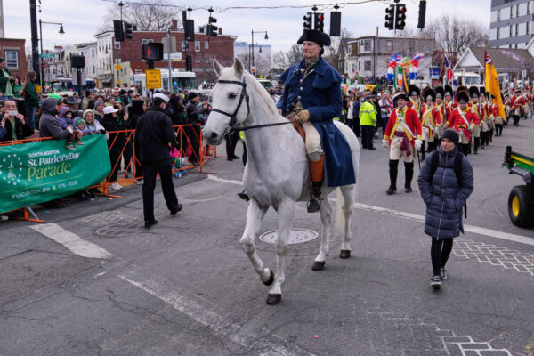 Boston crowd celebrating Massachusetts Evacuation Day 2026 with flags and parade atmosphere